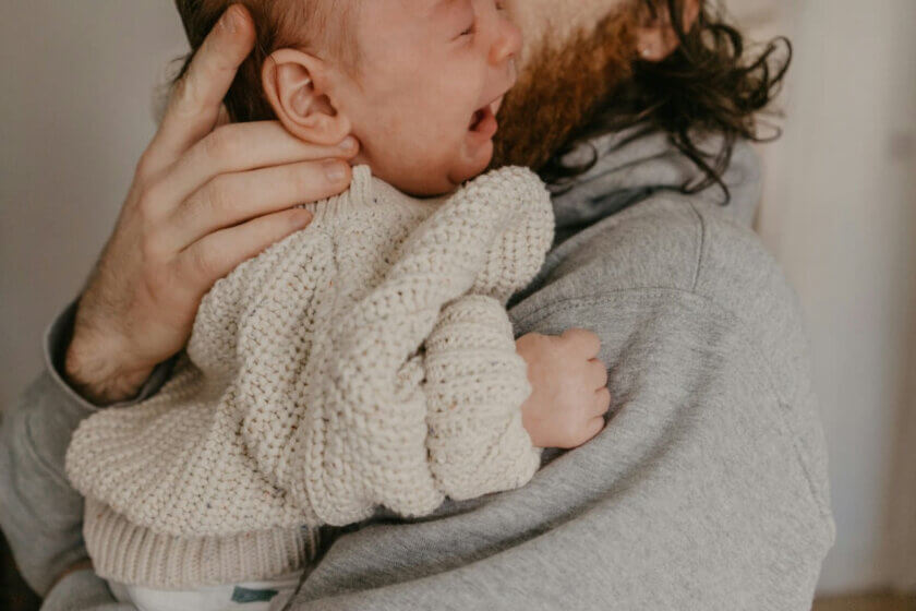 Baby beruhigen / Bezugsperson beruhigt ein weinendes Baby durch Nähe und sanften Körperkontakt.