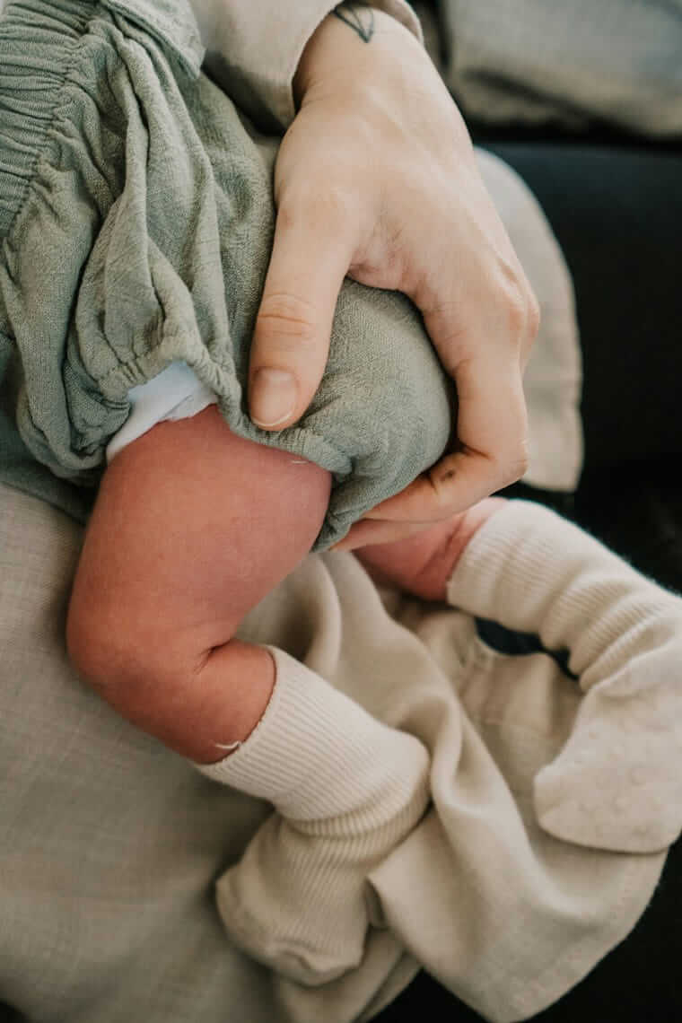 Baby beruhigen / Bezugsperson stützt sanft das Bein eines Babys und beruhigt es durch engen Körperkontakt.