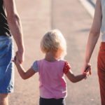 Sorgerecht / Kind hält die Hände von zwei erwachsenen Bezugspersonen beim gemeinsamen Gehen