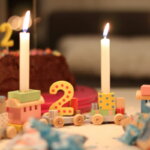 3. Lebensjahr, 2. Geburtstag / Geburtstagstisch mit Holzeisenbahn, der Zahl 2 und brennenden Kerzen vor einem Schokoladenkuchen