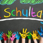Schulanfang, Einschulung, erster Schultag / viele angemalte Kinderhände mit Smileys vor Kreidetafel mit dem Wort "1. Schultag"