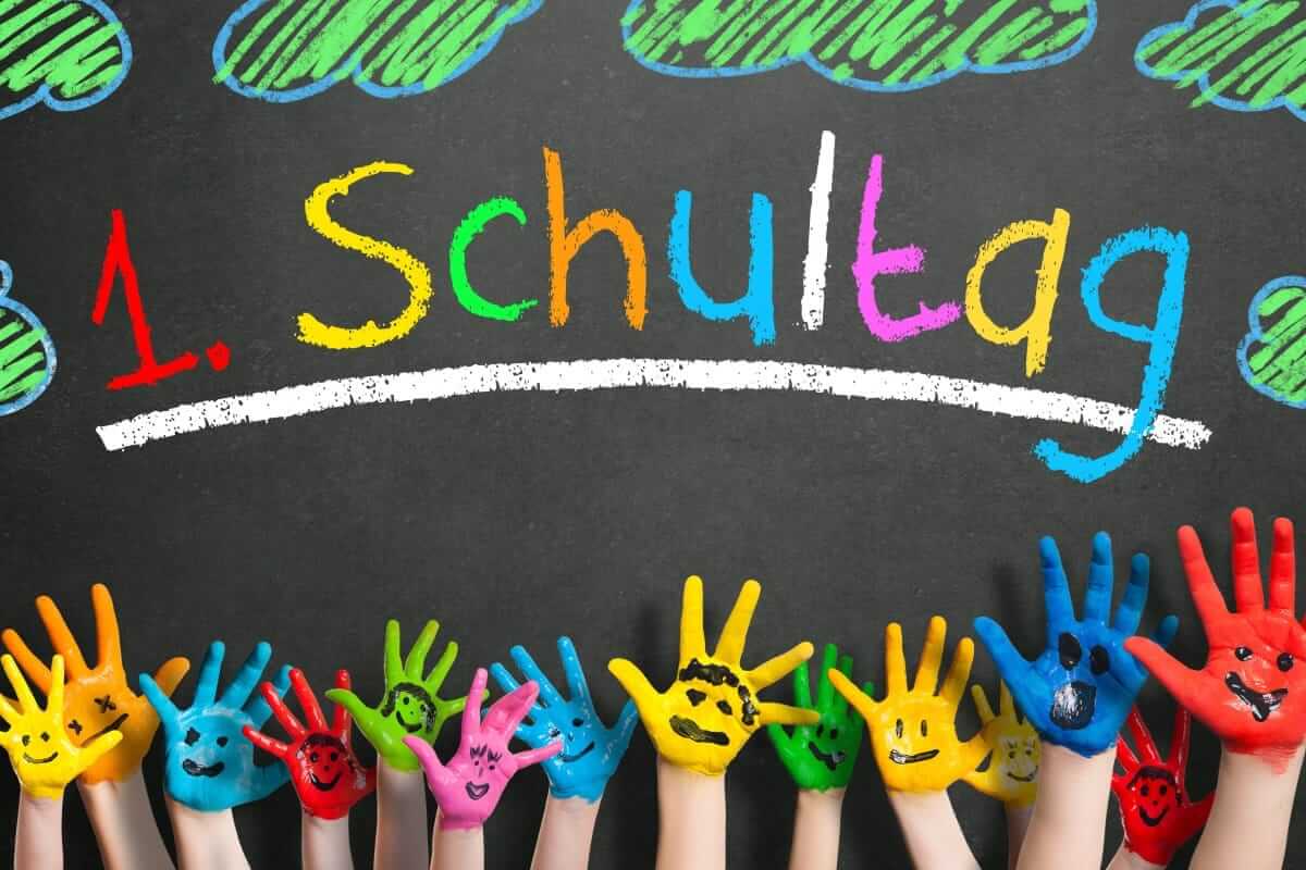 Schulanfang, Einschulung, erster Schultag / viele angemalte Kinderhände mit Smileys vor Kreidetafel mit dem Wort "1. Schultag"