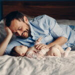 Fruchtbarkeit, Alter, späte Eltern (Portrait of middle age Caucasian father talking to newborn baby son daughter. Male man parent smiling to child on bed in bedroom at home.)