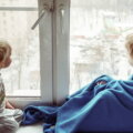 Kinderzimmerfenster, Fenster abdichten (Mädchen in Decke eingewickelt sitzt neben Jungen am Fenster)