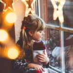 Nikolaus (Little preschool girl holding cup Santa Claus boot with gift called Nikolausstiefel in German. Happy child wait on holiday by window with Christmas lights in winter. Cozy family celebration of xmas.)
