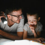Kindergarten, Kinderbücher, Vorlesen (Happy family reading bedtime story under blanket in evening. Father and son spend time together. )