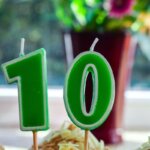 11. Lebensjahr, 10. Geburtstag / : Zwei grüne Geburtstagskerzen in Form der Zahl 10 stecken in einem Cupcake auf einer Fensterbank