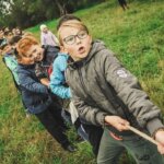 Klassengemeinschaft / Gruppe von Kindern beim Tauziehen auf einer Wiese – sie ziehen gemeinsam an einem Seil und lachen dabei. Symbol für Teamgeist, Zusammenhalt und Klassengemeinschaft.