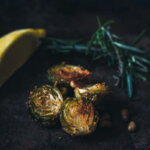 Winter-Superfoods / Gerösteter Rosenkohl mit knuspriger Kruste, Pinienkernen, Rosmarin und einer Zitronenscheibe auf dunklem Hintergrund.