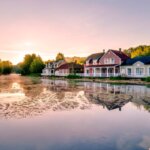 Ferienparks Holland, Center Parcs Niederlande / / Malerische Ferienhäuser am See bei Sonnenuntergang im Center Parcs – mit Spiegelung im Wasser und umgeben von grüner Natur.