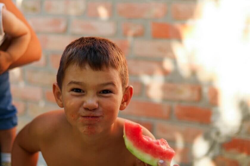 Essen bei Hitze (Lachender Junge isst ein Stück Wassermelone an einem warmen Sommertag)