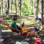 Spielen / Vier Kinder spielen draußen im Wald in einer Hängematte und genießen gemeinsam die Zeit in der Natur.