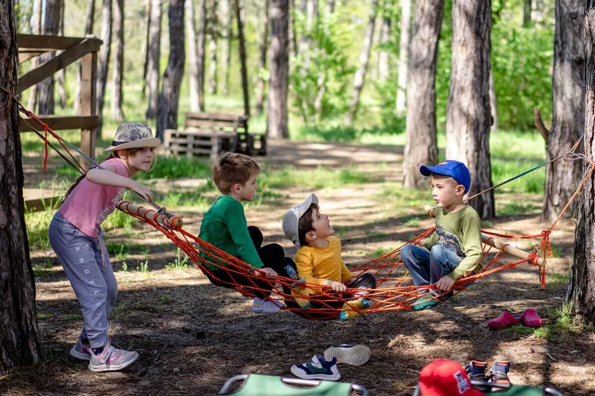 Spielen / Vier Kinder spielen draußen im Wald in einer Hängematte und genießen gemeinsam die Zeit in der Natur.
