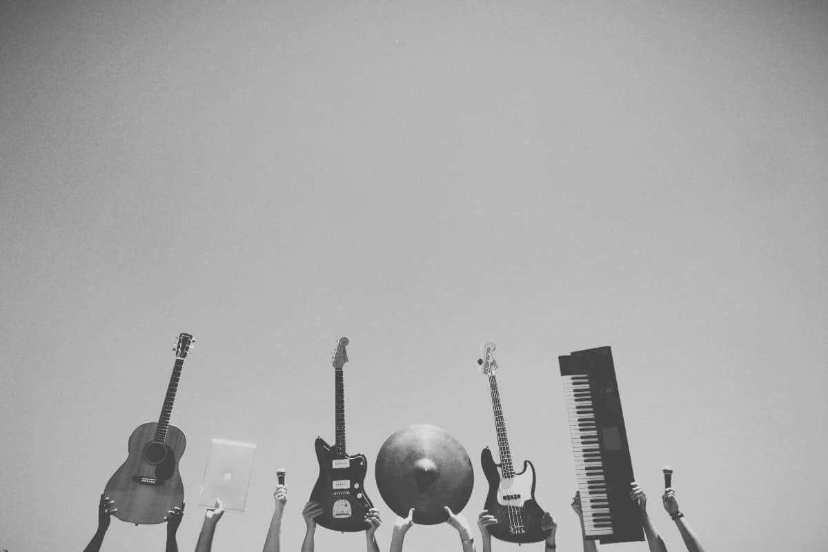 Weltmusiktag / Mehrere Menschen halten unterschiedliche Musikinstrumente wie Gitarre, Bass, Keyboard und Schlagzeug in den Himmel – Symbol für Vielfalt und Freude an Musik.