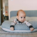 Baby liegt auf einem Stillkissen auf dem Bett und schaut neugierig in die Kamera