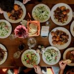 Gedeckter Tisch mit verschiedenen Tellern, Salaten und Brot – gemeinsames Abendessen von oben fotografiert