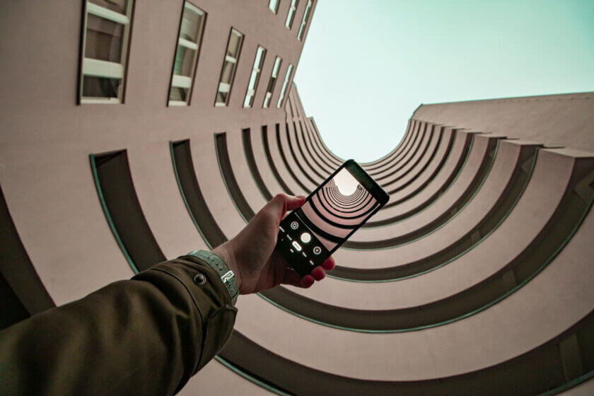 SIM-Only / Smartphone wird in einer Hand gehalten, im Hintergrund eine moderne Gebäudestruktur