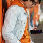 Kinder im Internet (Teenager in weißer Jacke mit Smartphone vor Graffiti-Wand)