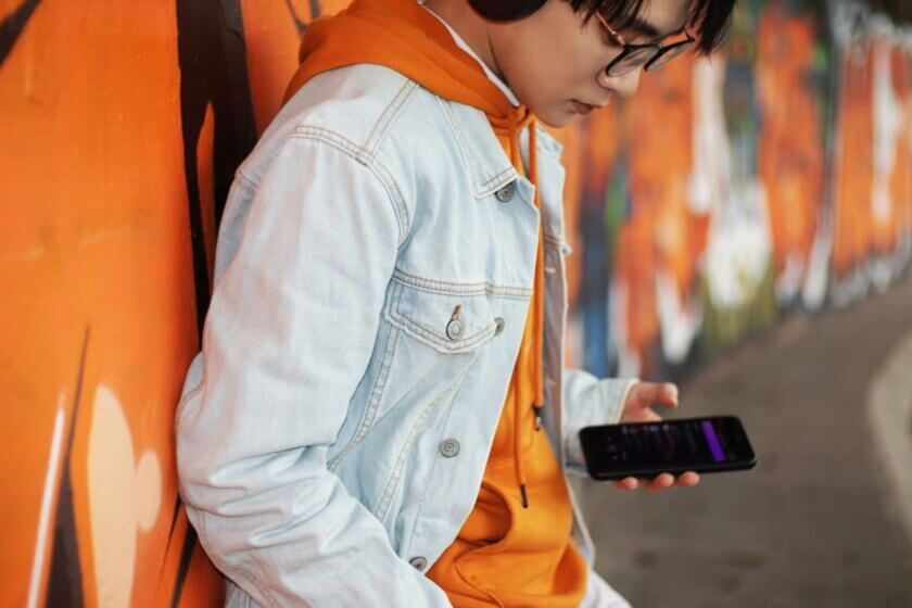 Kinder im Internet (Teenager in weißer Jacke mit Smartphone vor Graffiti-Wand)