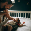 Reizhusten / Vater beugt sich nachts über das Gitterbett seines Babys