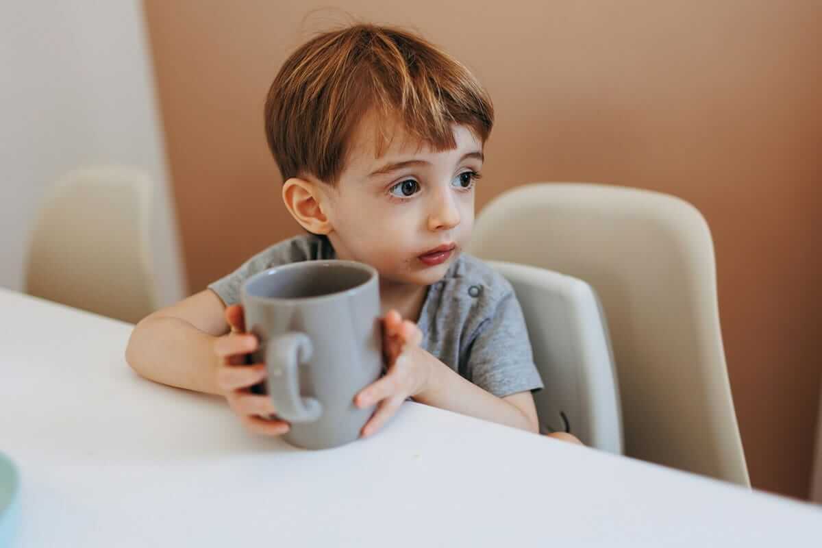 Reizhusten / Kleinkind sitzt am Tisch und hält eine Tasse mit beiden Händen