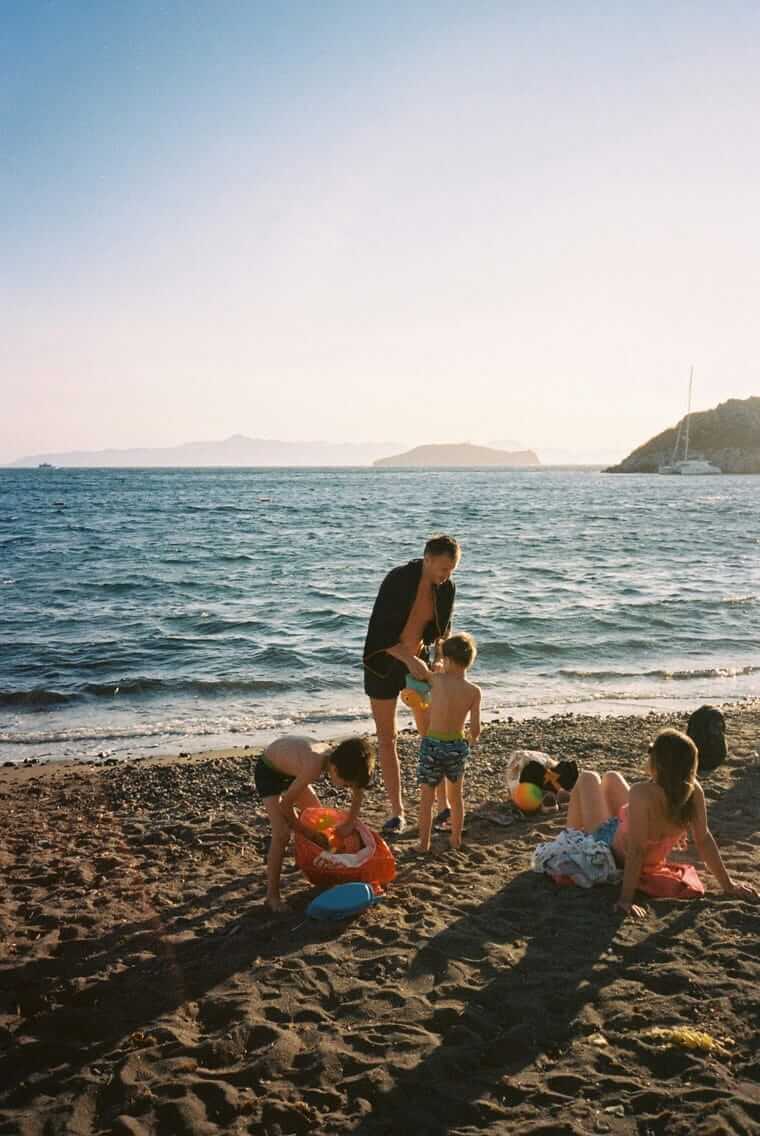 Familie spielt mit mehreren Kindern am Strand – jedes Kind beschäftigt sich anders beim Familienurlaub
