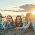 Fünf Geschwister unterschiedlichen Alters liegen zusammen auf einer Wiese bei Sonnenuntergang – Familienurlaub mit mehreren Kindern
