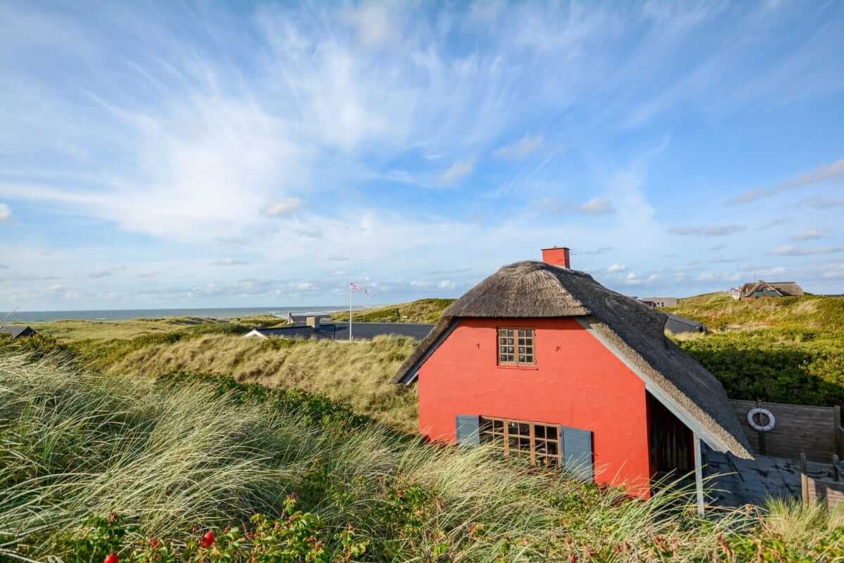 Traditionelles rotes Ferienhaus mit Reetdach in den Dünen von Blavand, Dänemark