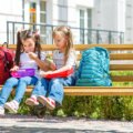 Zwei Grundschulkinder sitzen auf einer Schulbank und öffnen gemeinsam ihre Brotdosen in der Pause