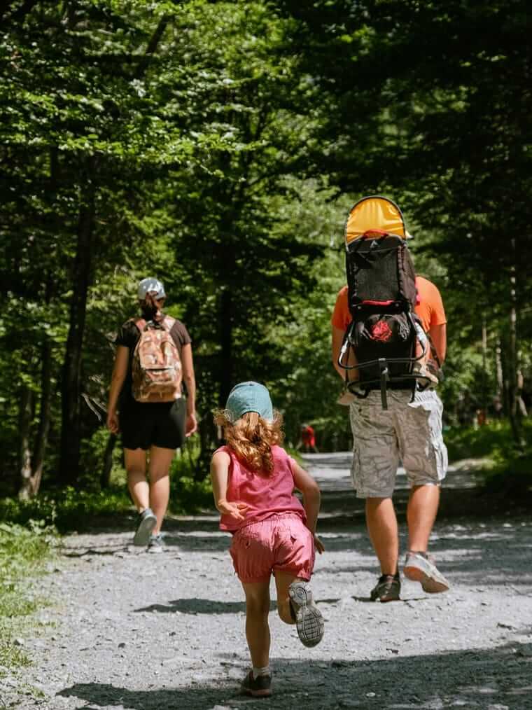 Familie wandert mit Kleinkind in der Rückentrage durch den Wald – die richtige Ausrüstung erleichtert den Bergurlaub