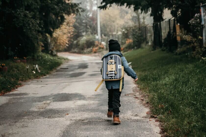 Schulwechsel / Kind mit Schulranzen läuft allein einen Herbstweg entlang