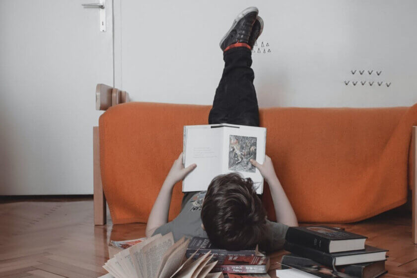 Lernen ohne Stress / Junge liegt entspannt zwischen Büchern und liest auf dem Boden