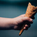 Kinderhand hält eine fast aufgegessene Eiswaffel vor dunklem Hintergrund – nur ein kleiner Rest ist übrig