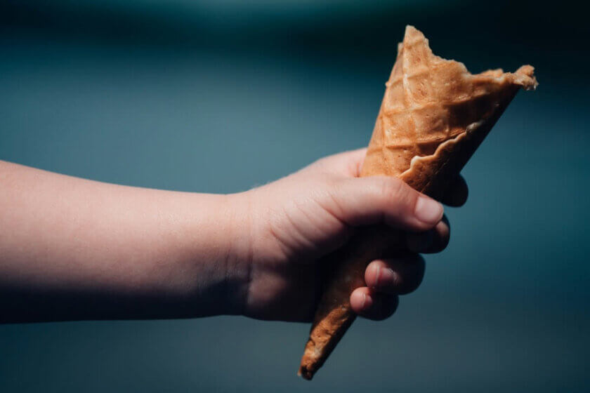 Kinderhand hält eine fast aufgegessene Eiswaffel vor dunklem Hintergrund – nur ein kleiner Rest ist übrig