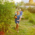 Sommerferien mit Kindern / Kinder rennen mit Wasserpistolen durch einen sommerlichen Garten im Abendlicht