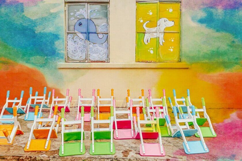 Kita / Bunte Kinderstühle aufgereiht vor einer farbenfrohen Hausfassade mit gemalten Tiermotiven auf den Fenstern einer Kindertagesstätte