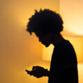 Teenager / Jugendliche Person im Gegenlicht einer Stehlampe, Blick aufs Smartphone – Symbol für den digitalen Rückzug in der Pubertät.