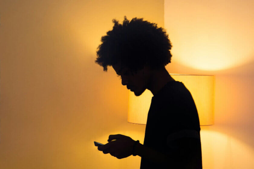 Teenager / Jugendliche Person im Gegenlicht einer Stehlampe, Blick aufs Smartphone – Symbol für den digitalen Rückzug in der Pubertät.