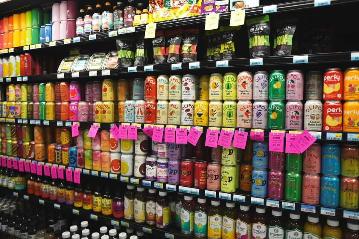„Mama, kaufst du mir das?“ – Wie Werbung die Wünsche unserer Kinder beeinflusst Vollständig gefüllte Supermarktregalwand mit bunten Getränkedosen in allen Farben – Symbol für die Reizüberflutung durch Produktwerbung im Alltag.