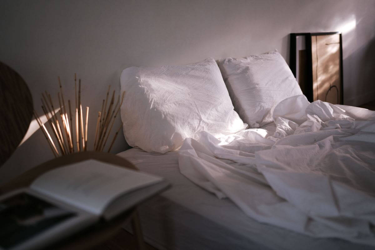 Spannbettlaken: kühlend und sanft für einen schönen Schlaf im Sommer Ungemachtes Bett mit weißer Leinenbettwäsche im Morgenlicht – sommerliche Schlafatmosphäre mit luftigen Textilien.