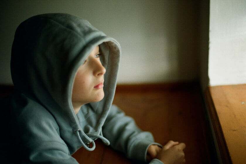 Leistungsdruck / Junge im Hoodie sitzt nachdenklich am Fenster