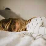 Kind liegt mit Haaren im Gesicht wach im Bett – Schlafprobleme bei Schulkindern