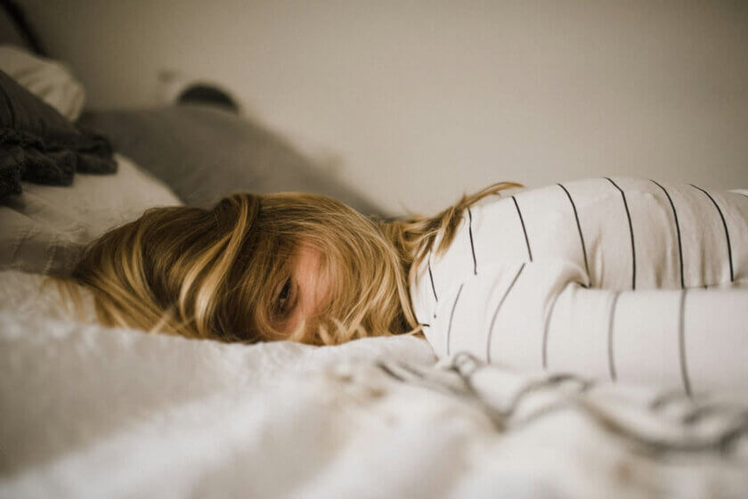 Kind liegt mit Haaren im Gesicht wach im Bett – Schlafprobleme bei Schulkindern