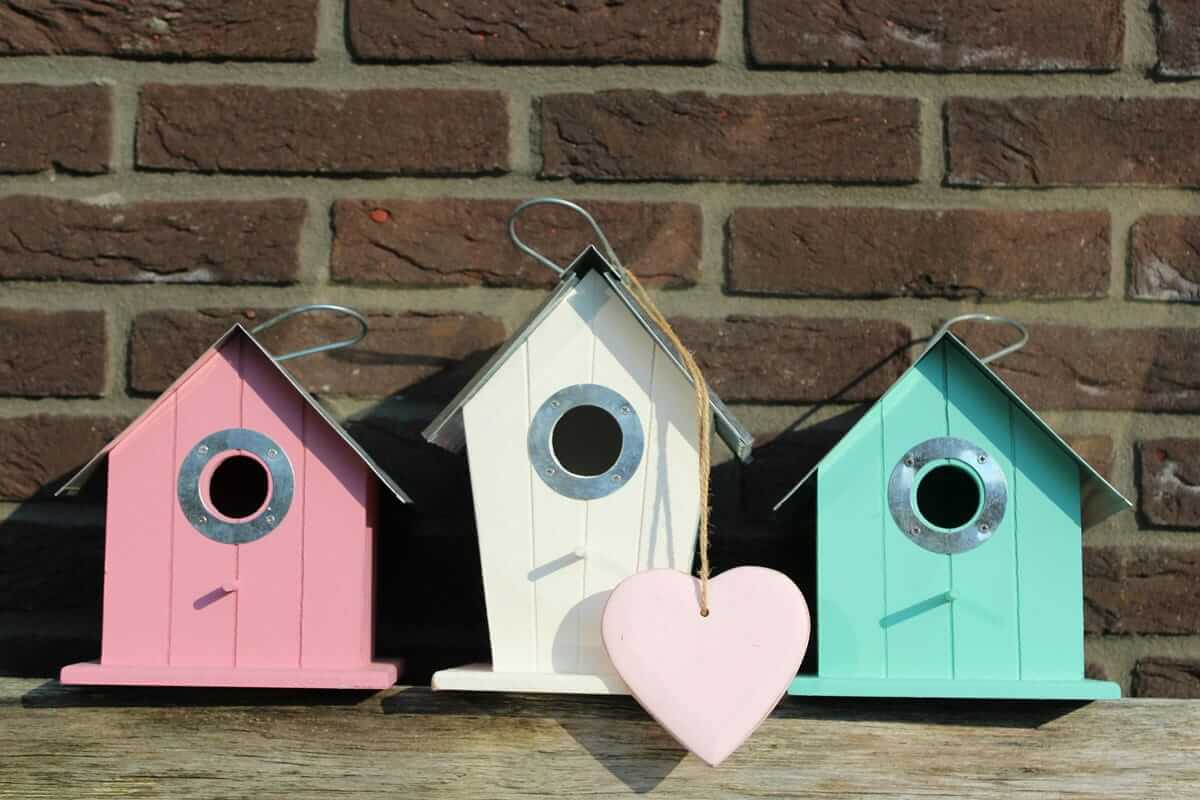 Nesting-Party als entspannte Alternative zur Babyparty Nesting-Party / Drei bunte Vogelhäuschen in Rosa, Weiß und Türkis an einer Backsteinwand, in der Mitte hängt ein Herz aus Holz.